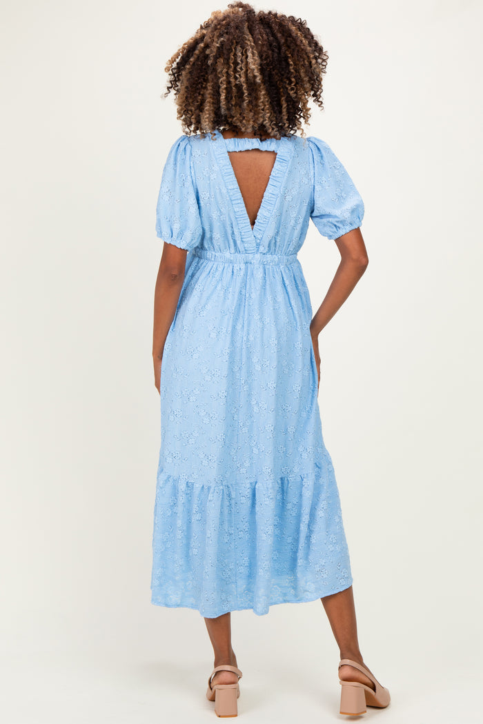 woman wearing a sky blue maternity dress with puffed sleeves and a tiered skirt, showing the back view