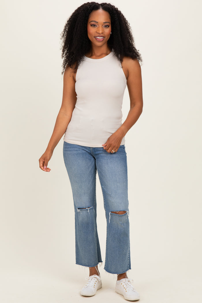 woman wearing a beige sleeveless ribbed top and light blue flared jeans with ripped knees
