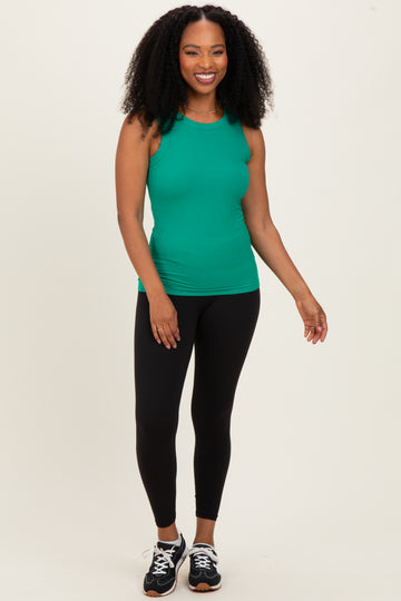 woman wearing a green ribbed tank top and black leggings, standing with a smile and sporty shoes