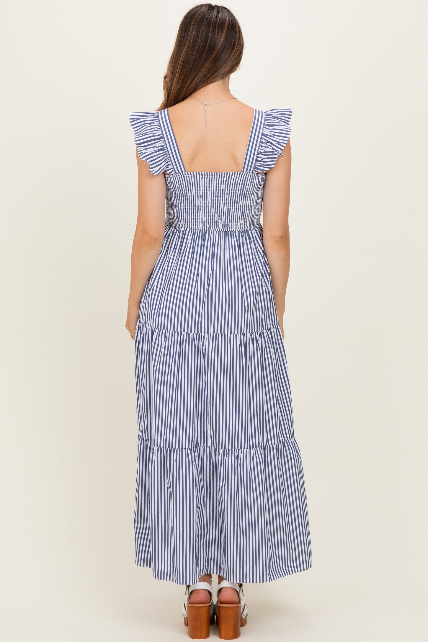 woman wearing a navy and white striped maternity maxi dress with ruffle straps and a tiered skirt