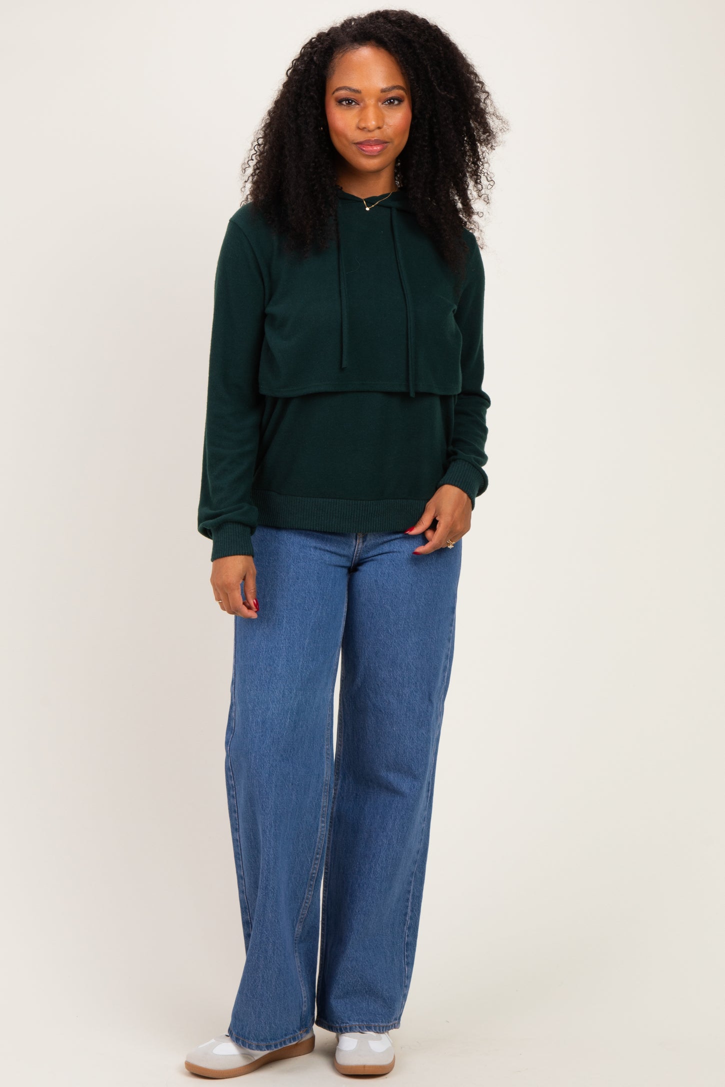 woman wearing a dark green cropped hoodie with a drawstring and wide-leg blue jeans