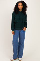 woman wearing a dark green cropped hoodie with a drawstring and wide-leg blue jeans
