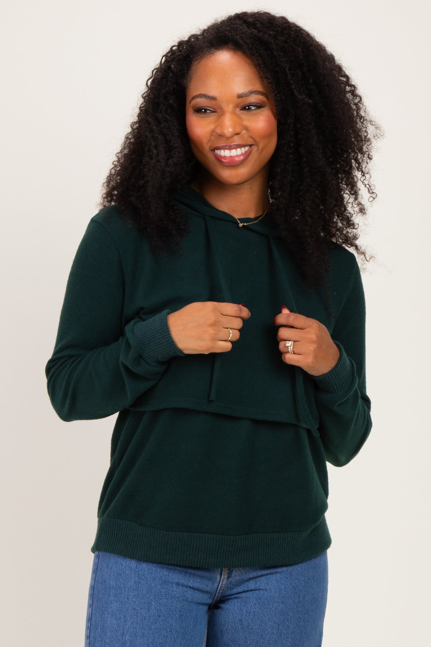woman wearing a dark green layered hoodie with a drawstring and a relaxed fit paired with blue jeans