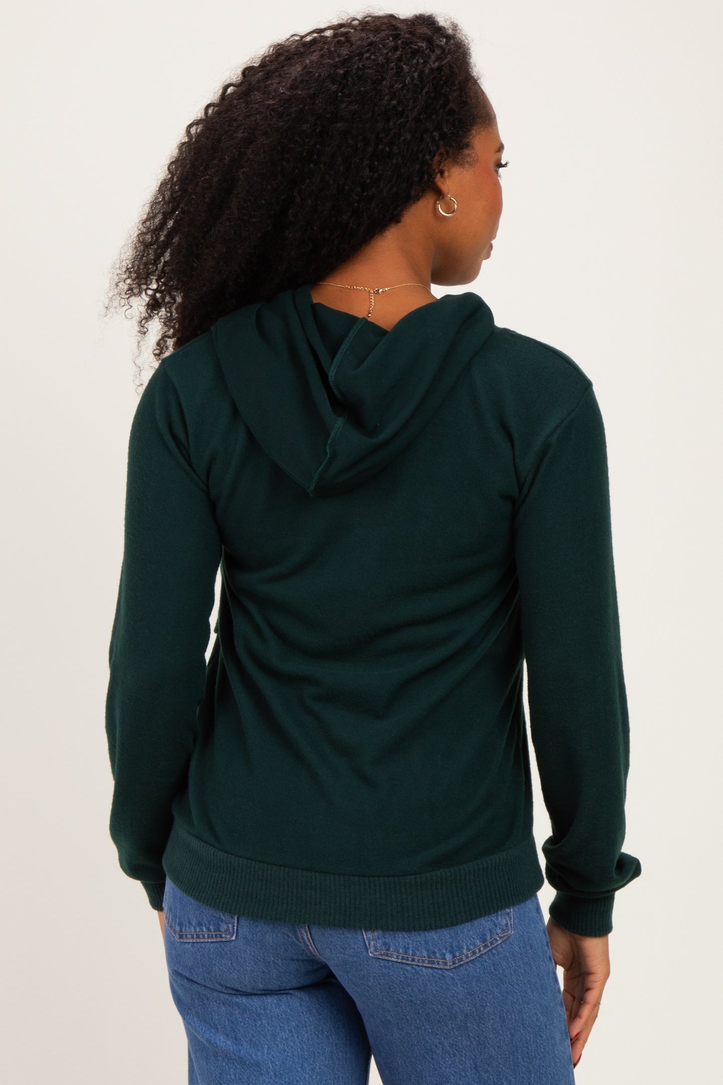 woman wearing a dark green hooded sweatshirt, seen from the back, with a relaxed fit and cuffed sleeves