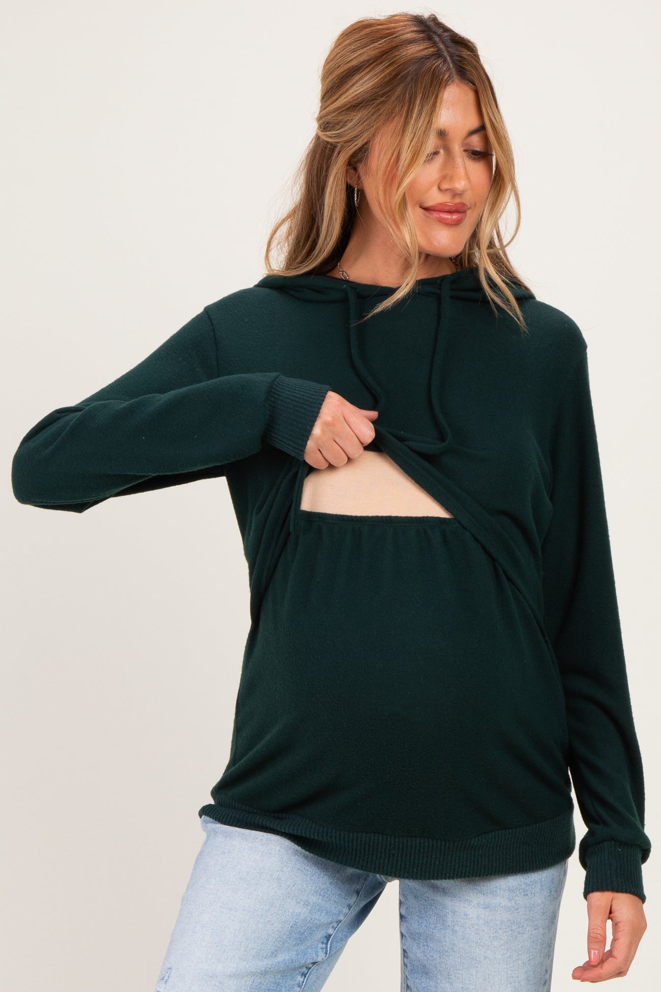 woman wearing a dark green maternity hoodie with a cutout for easy nursing and showing her baby bump