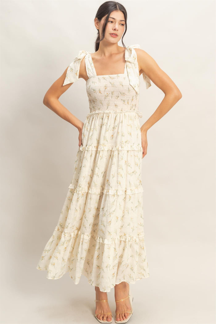 woman wearing a light yellow floral maxi dress with tie straps and a tiered skirt