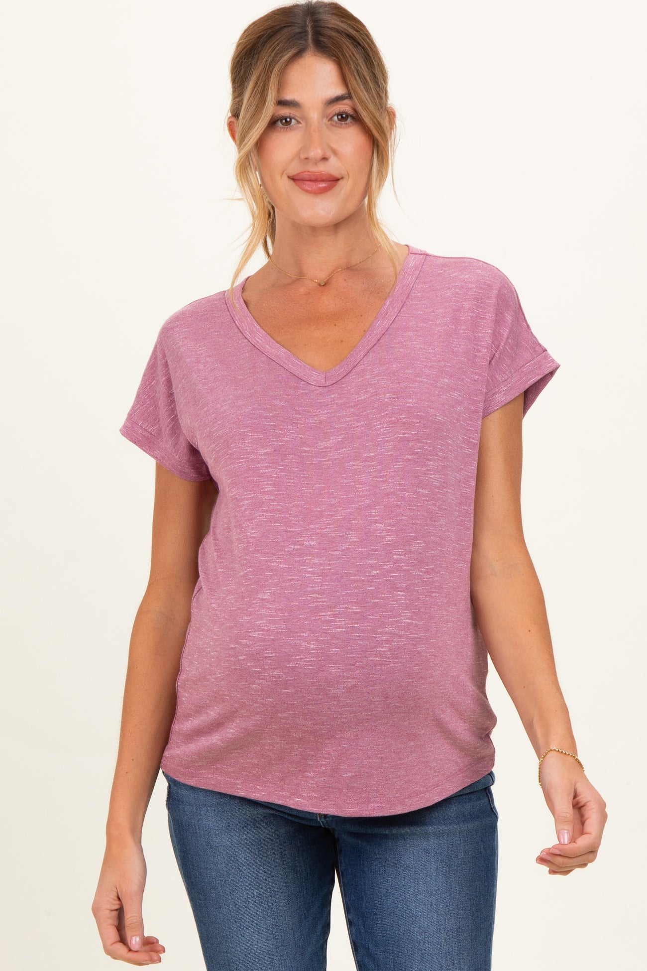woman wearing a raspberry v-neck maternity top with rolled sleeves and a visible baby bump, paired with jeans