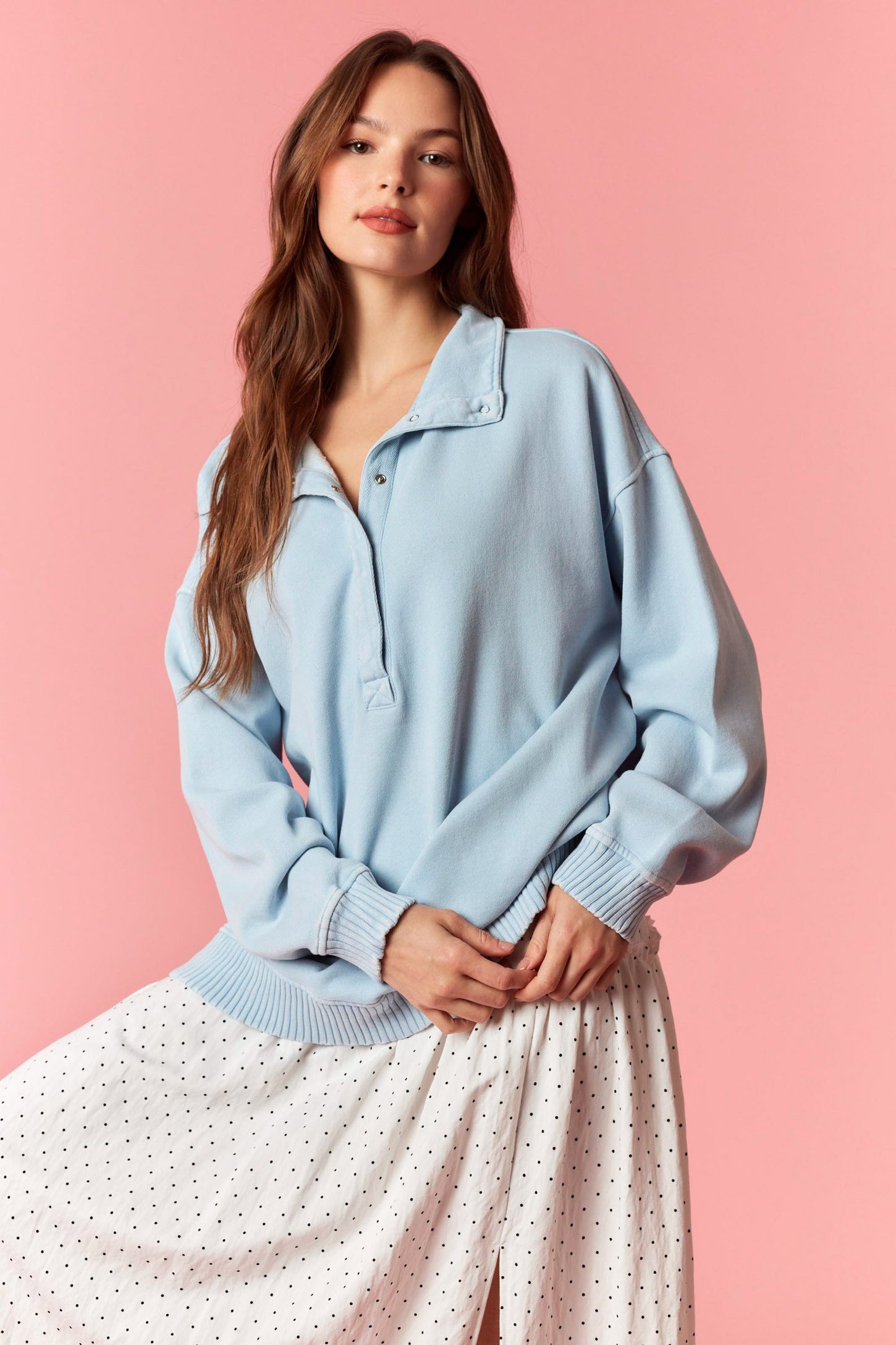 woman wearing a light blue oversized pullover with a collar and front buttons, paired with a white dotted skirt