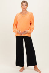 woman wearing an orange maternity top with long sleeves and a v-neck, paired with black wide-leg maternity pants and holding her baby bump
