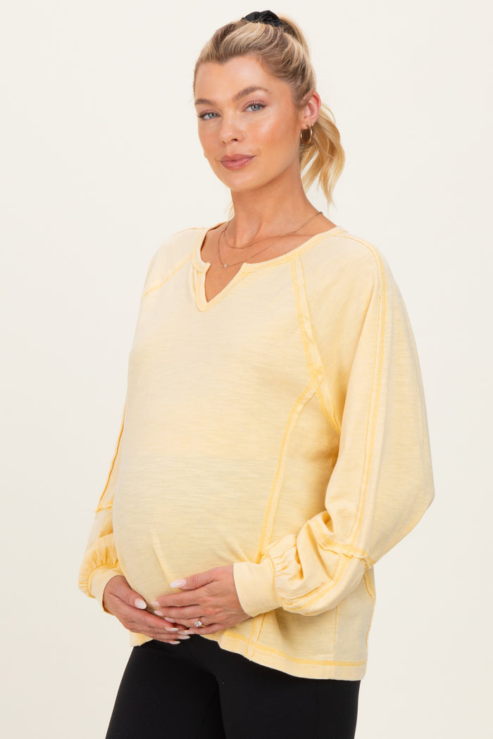 woman wearing a yellow maternity sweatshirt with a v-neck and balloon sleeves, gently cradling her baby bump