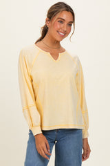 woman wearing a yellow long sleeve top with a v-neck and raglan sleeves, paired with light blue jeans