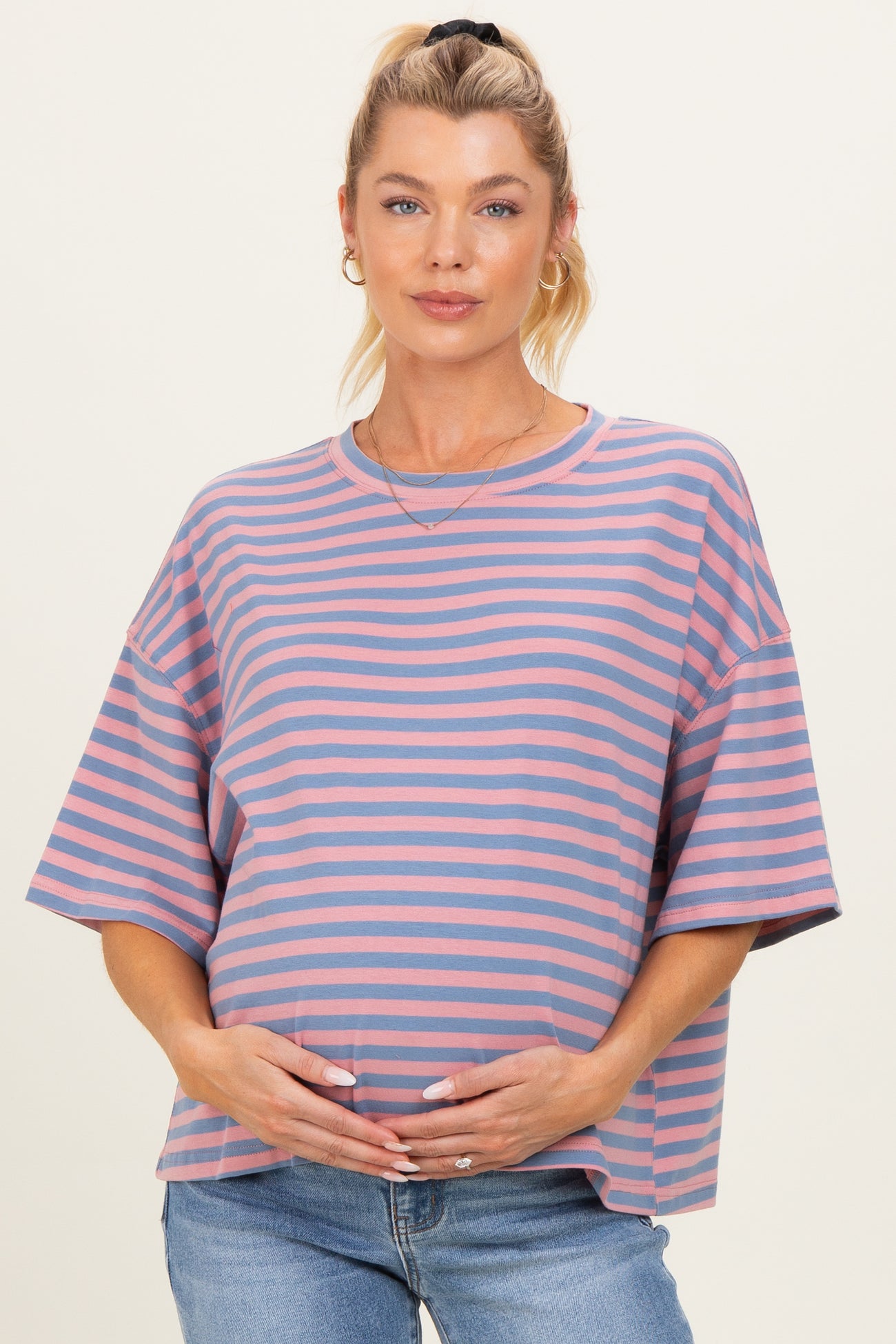woman wearing a pink and blue striped maternity top and holding her baby bump