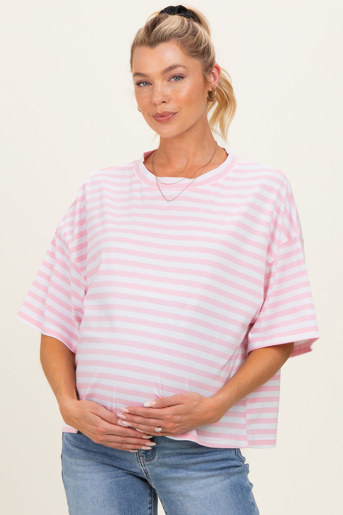 woman wearing a pink and white striped maternity top and holding her baby bump
