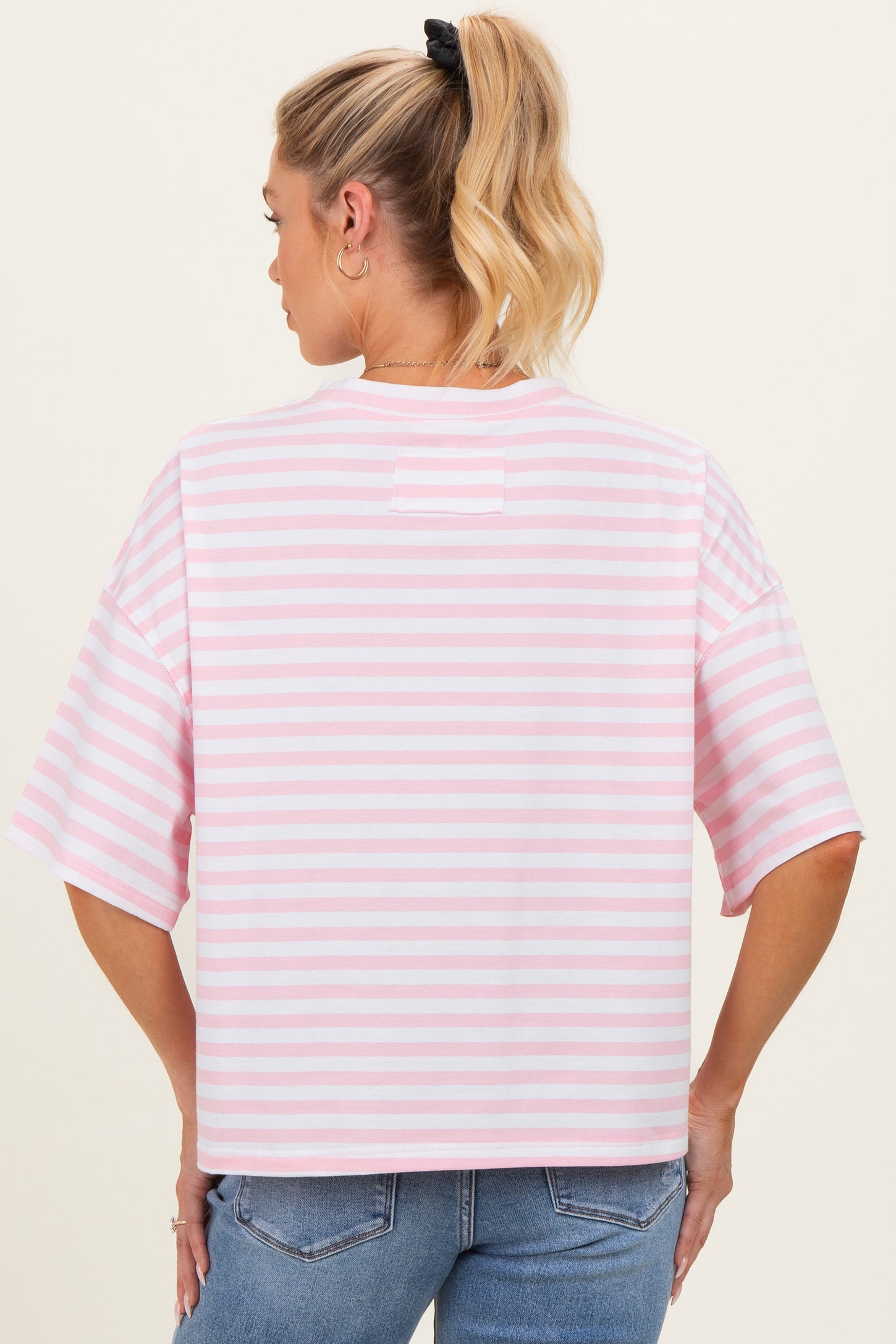 woman wearing a pink and white striped maternity top with short sleeves and a relaxed fit, showing her back