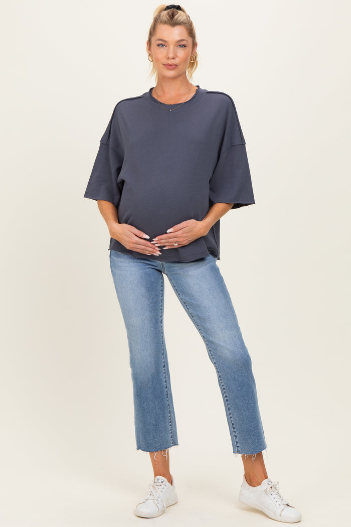 woman wearing a dark grey oversized maternity sweatshirt and light blue jeans, holding her baby bump