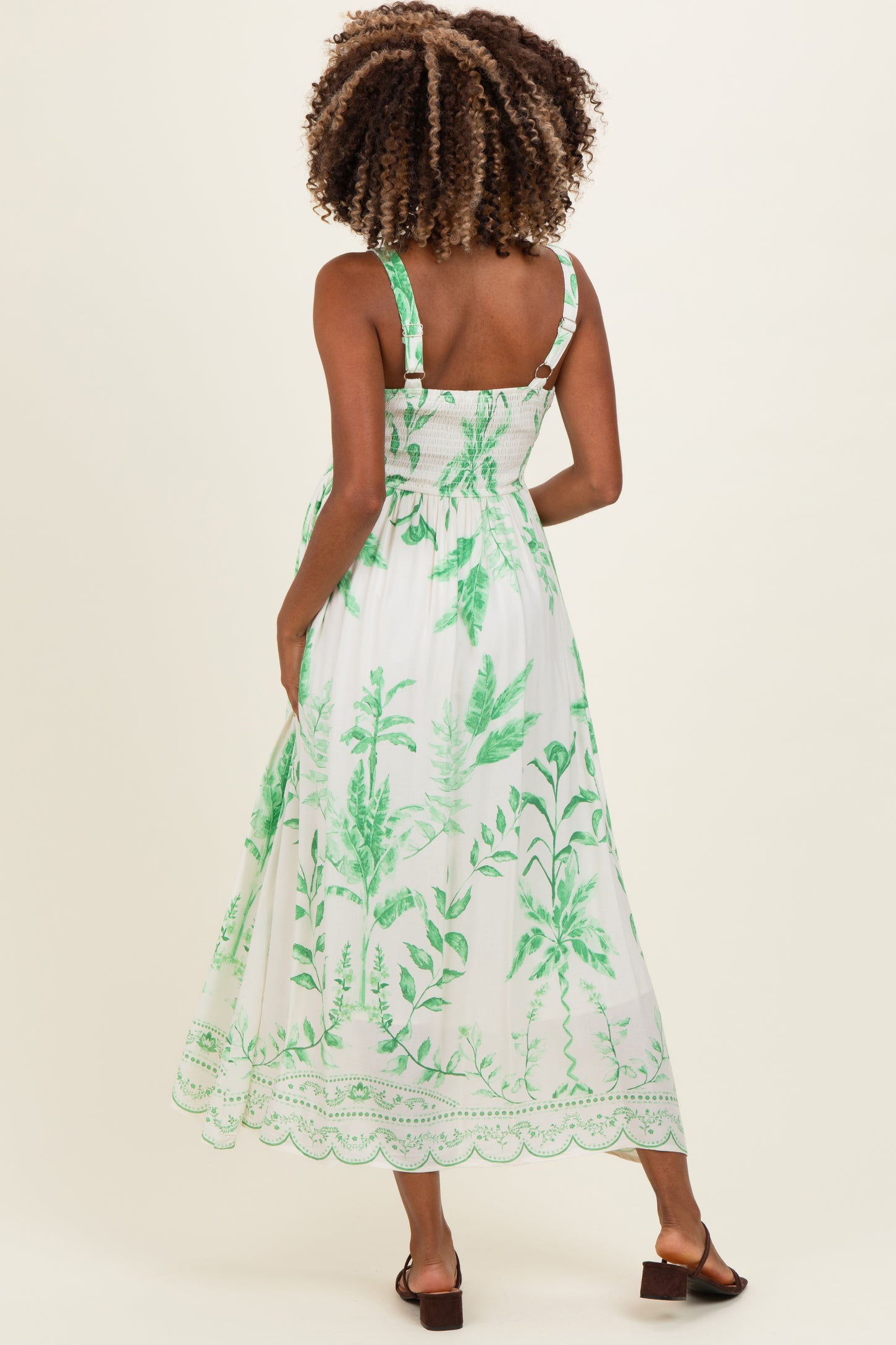 woman wearing a white maternity maxi dress with green leaf patterns and adjustable straps, showing a baby bump