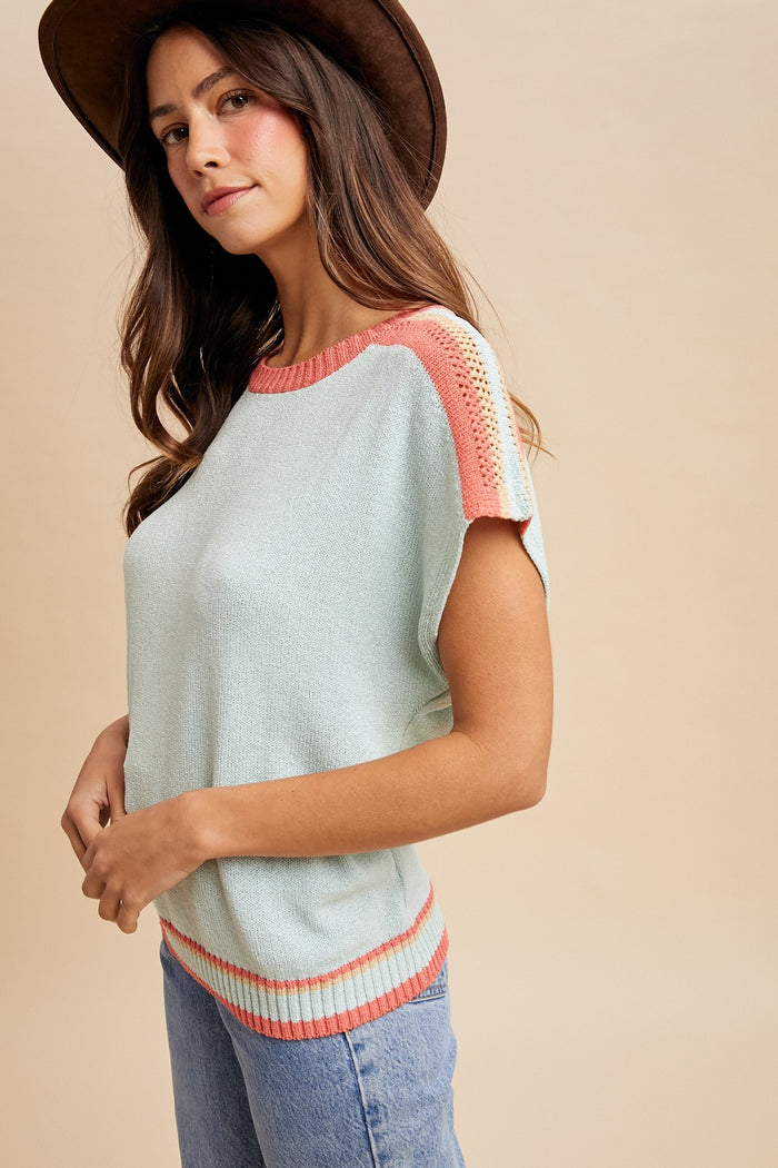 woman wearing a light blue short sleeve sweater with coral accents and wearing a brown hat