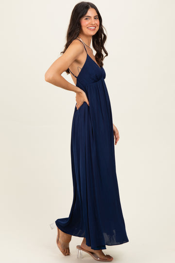 woman wearing a navy blue maxi dress with a halter neck and flowy skirt, smiling while standing sideways