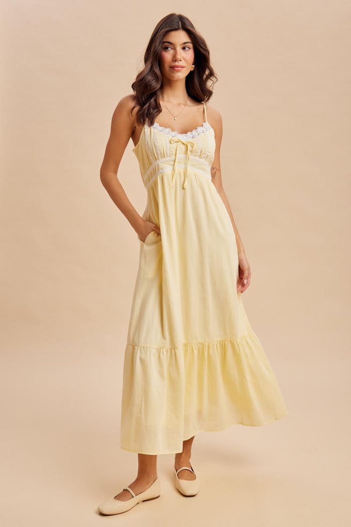 woman wearing a yellow maxi dress with lace detail and pockets, standing against a neutral background