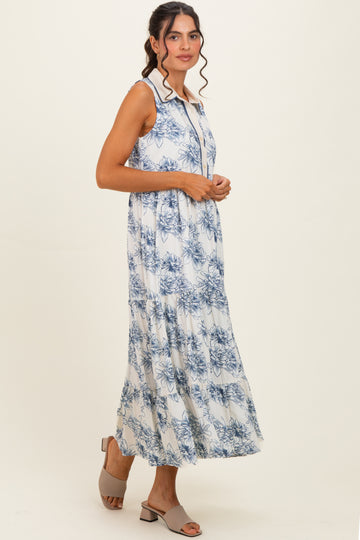 woman wearing a sleeveless white maxi dress with blue floral print and a tiered skirt, paired with gray heeled sandals