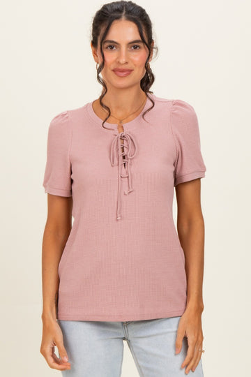 woman wearing a pink short sleeve top with puff sleeves and lace-up detail in the front