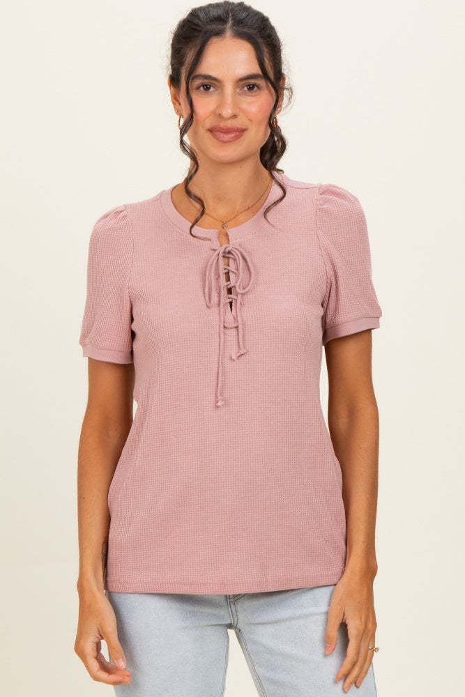 woman wearing a pink short sleeve top with puff sleeves and lace-up detail in the front