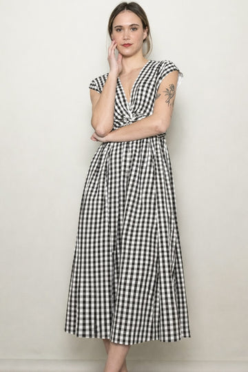 woman wearing a black and white gingham midi dress with cap sleeves and a cinched waist standing against a plain background