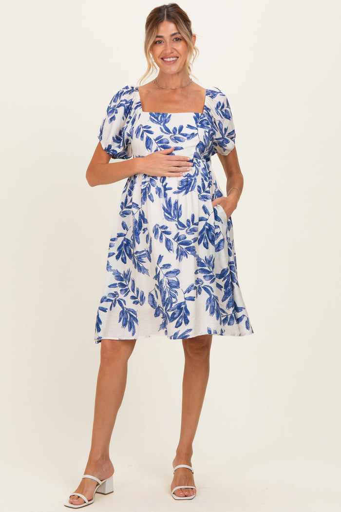 woman wearing a blue and white floral print maternity dress with puff sleeves and pockets, holding her baby bump