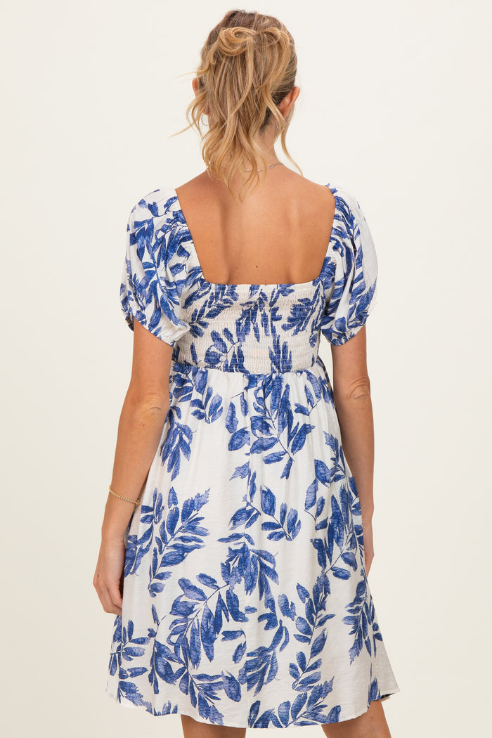 woman wearing a white maternity dress with blue floral print and puffed sleeves, showing the back view