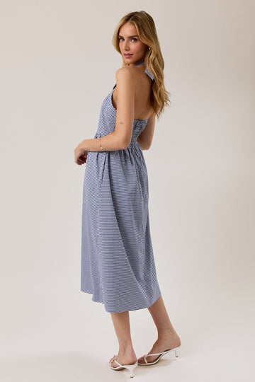 woman wearing a blue and white gingham halter neck mid-length dress, standing with her back to the camera