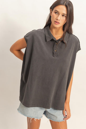 woman wearing a dark gray oversized polo shirt with a button placket and paired with distressed denim shorts