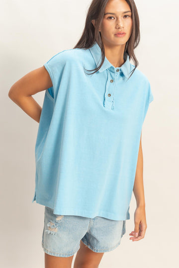 woman wearing a light blue sleeveless polo shirt with three buttons and distressed denim shorts
