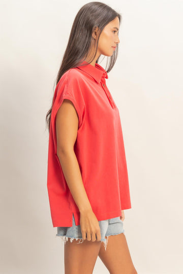 woman wearing a coral oversized polo shirt with short sleeves and side slits, paired with distressed denim shorts