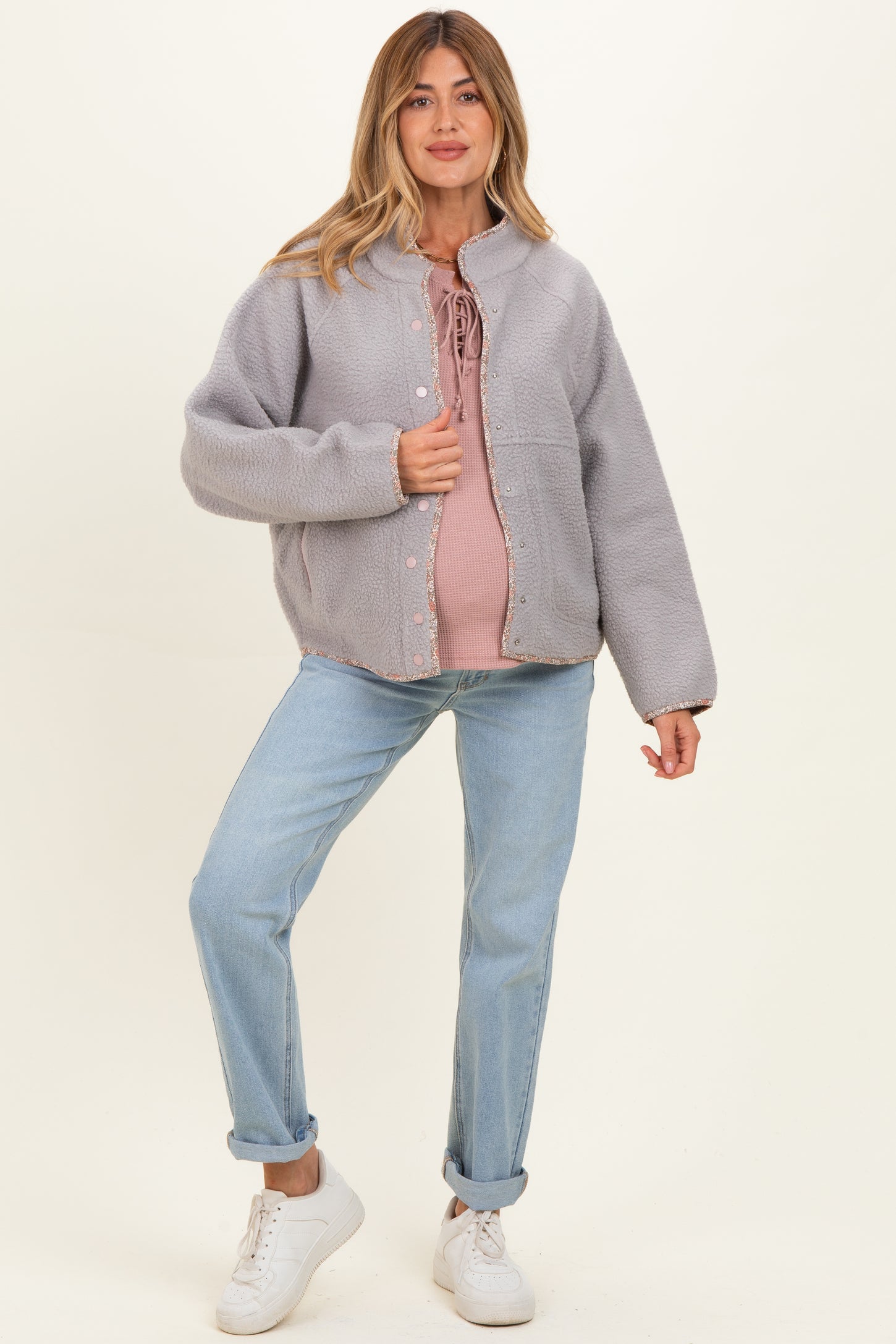 woman wearing a light gray fleece maternity jacket over a pink top and blue jeans, with a visible baby bump