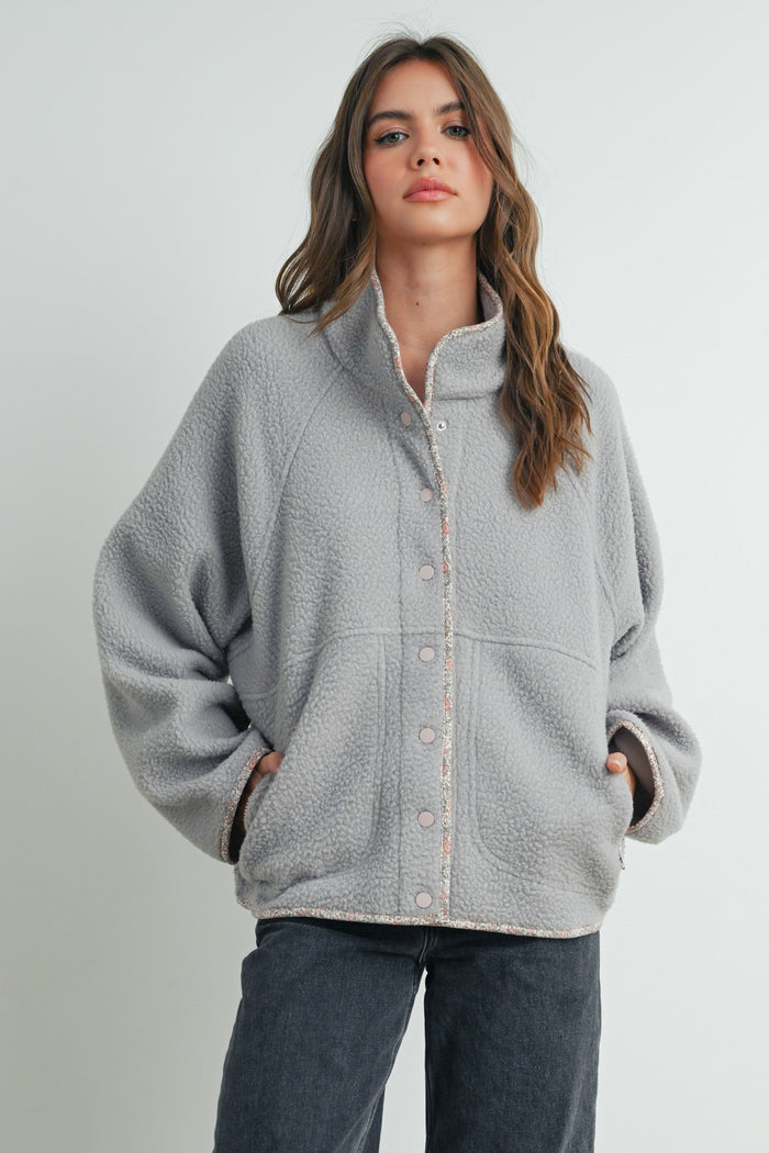 woman wearing a cozy gray fleece jacket with a button-down front and side pockets