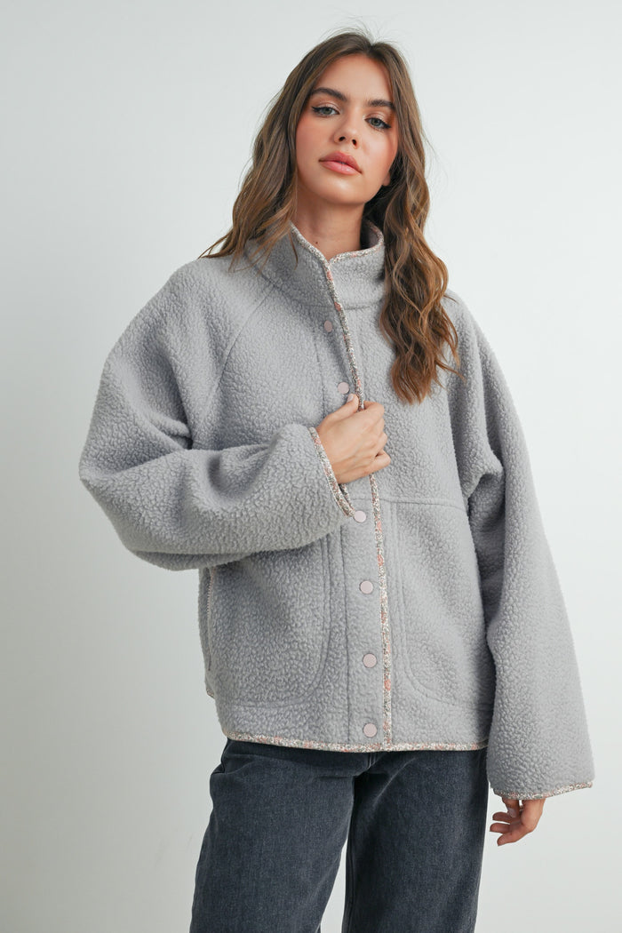 woman wearing a gray fleece jacket with a button front and oversized sleeves, paired with dark jeans