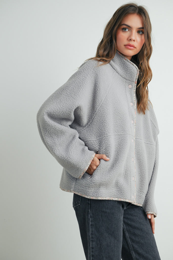 woman wearing a grey fleece jacket with a high collar and snap buttons, paired with black jeans