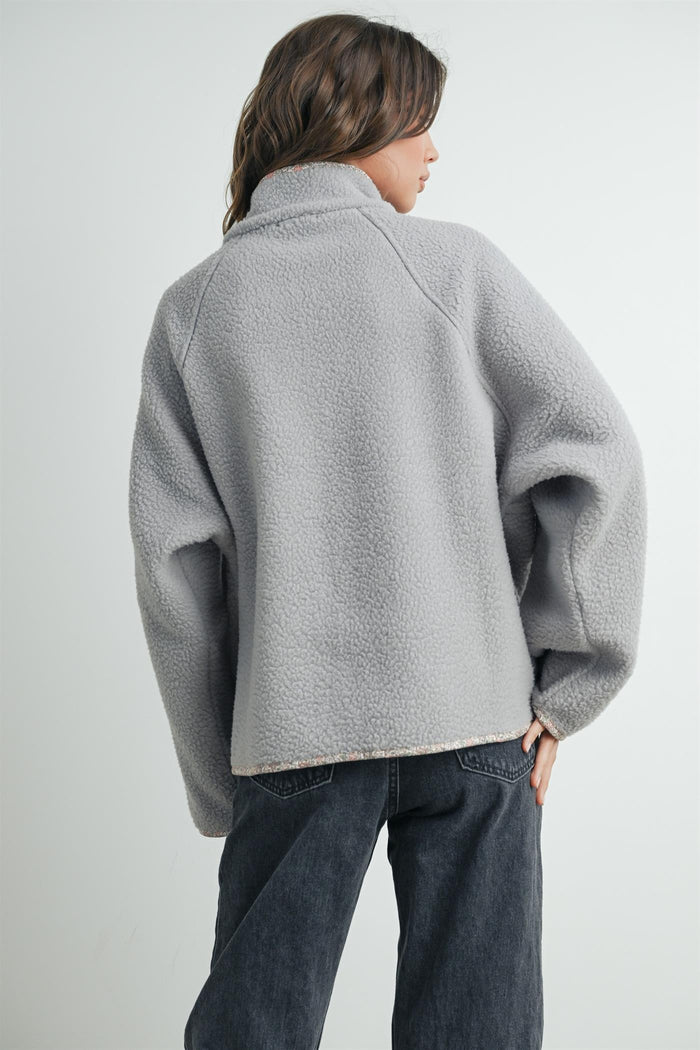 woman wearing a gray fleece pullover with a mock neck and oversized fit, facing away from the camera