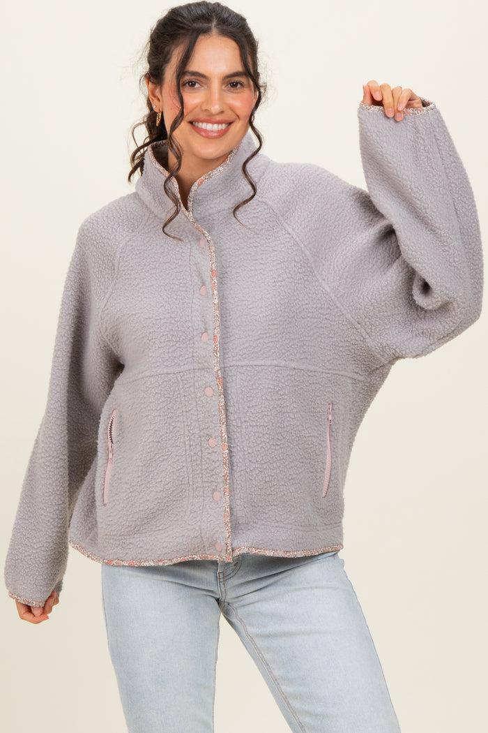 woman wearing a grey fleece jacket with a high collar and button front, styled with pink accents and pockets