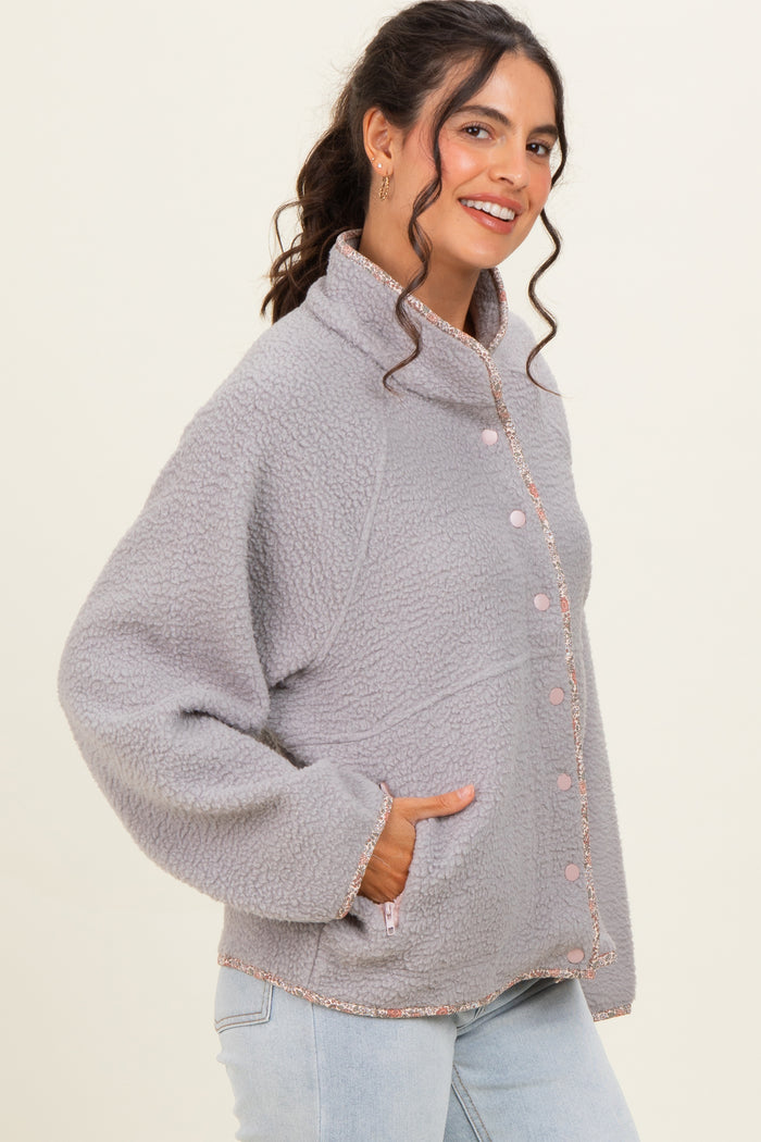 woman wearing a light gray fleece jacket with pink buttons and trim, featuring side pockets and a relaxed fit