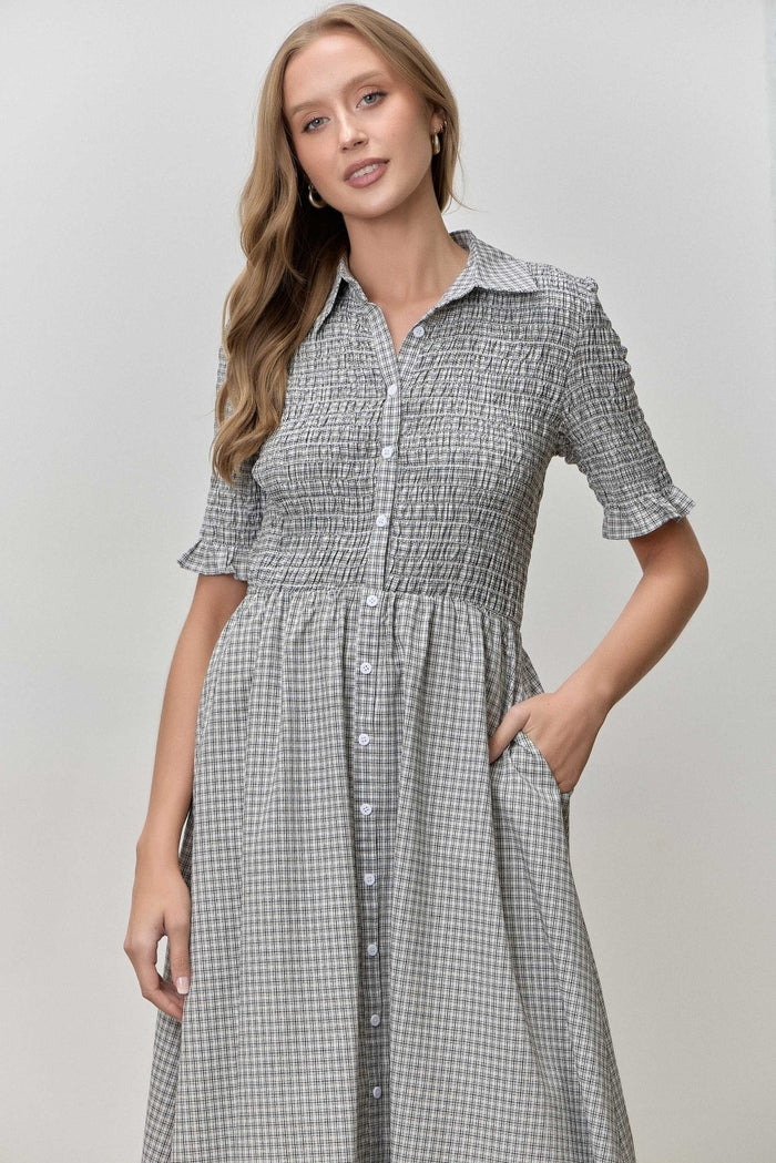 woman wearing a black and white gingham button-up dress with short sleeves and a smocked bodice, standing with one hand in her pocket