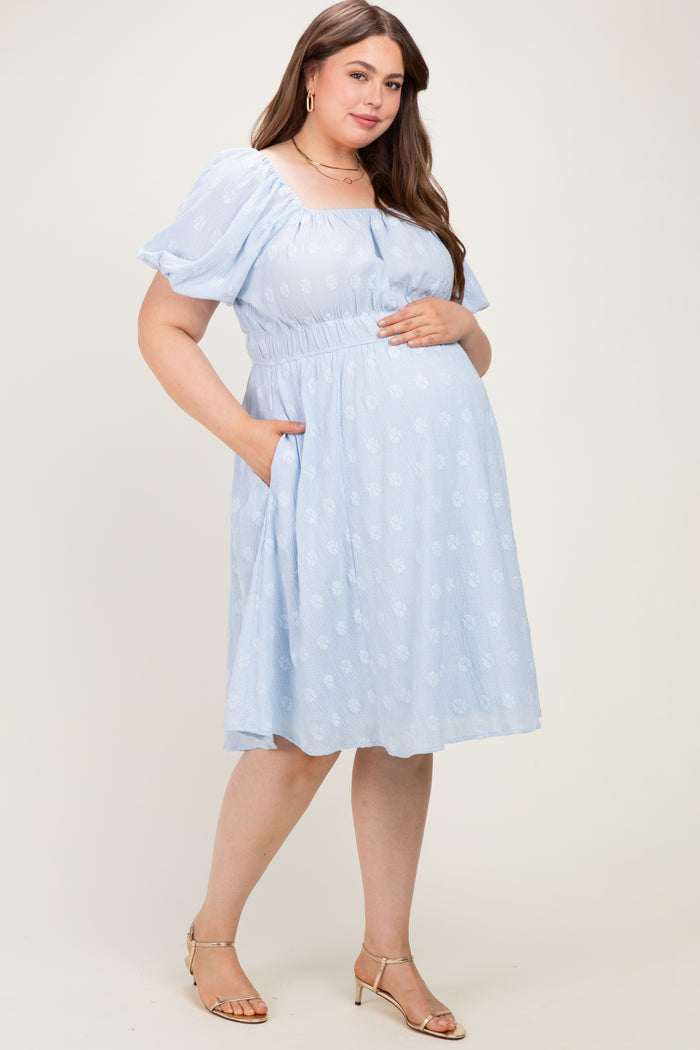 woman wearing a light blue floral maternity dress with short puff sleeves and pockets, holding her baby bump