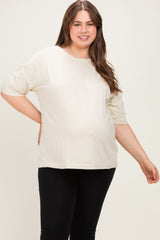 woman wearing a light beige short sleeve maternity top with a visible baby bump and black leggings