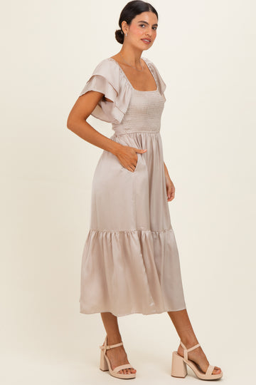 woman wearing a beige satin midi dress with ruffled sleeves and pockets, standing on a light background