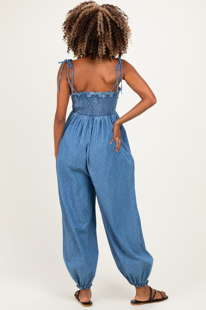 woman wearing a blue denim maternity jumpsuit with smocked bodice and tied straps, showing off her baby bump from the back