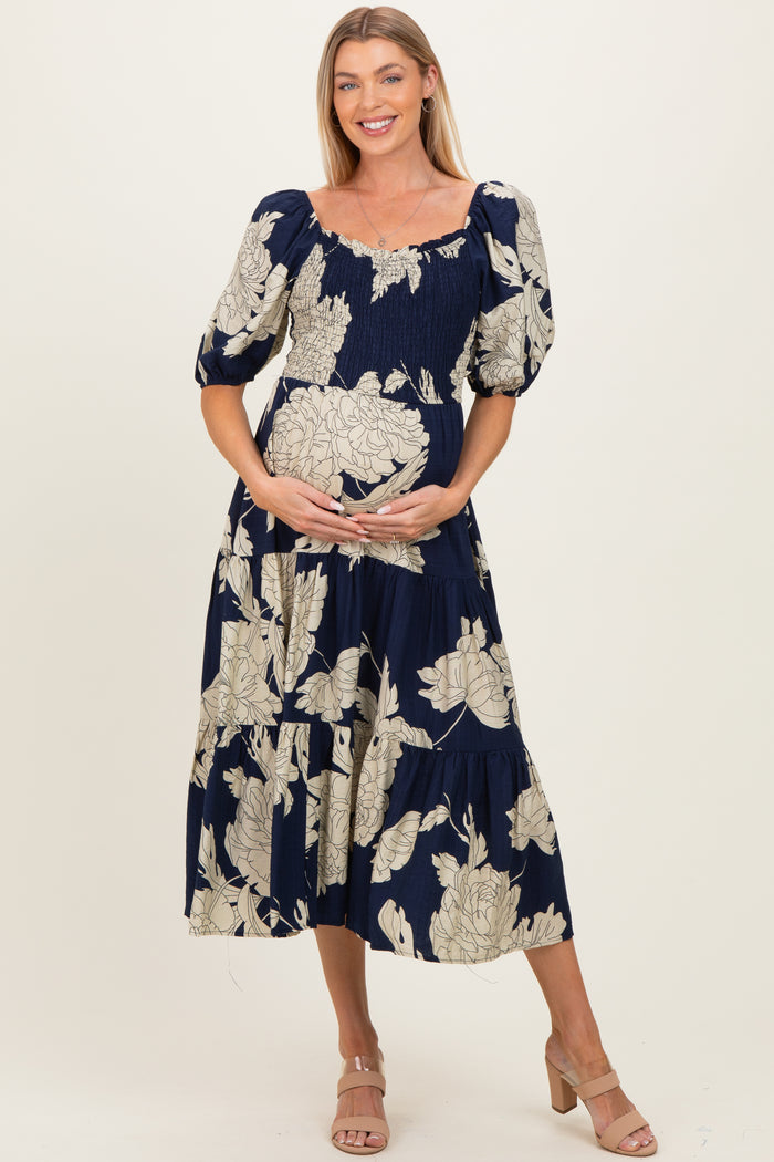 woman wearing a navy blue floral maternity dress with puff sleeves, holding her baby bump