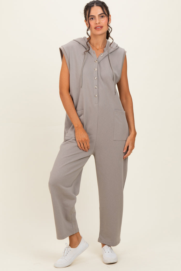 woman wearing a gray sleeveless jumpsuit with a hood and button details, standing against a neutral background