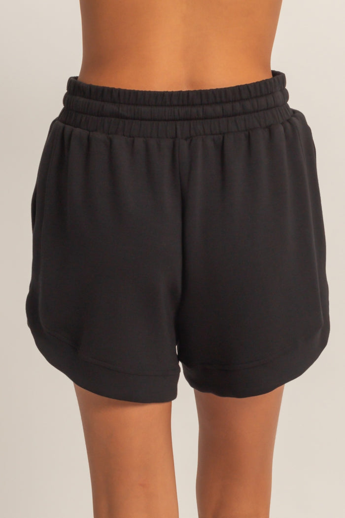 black women's athletic shorts with an elastic waistband and curved hem, shown from the back