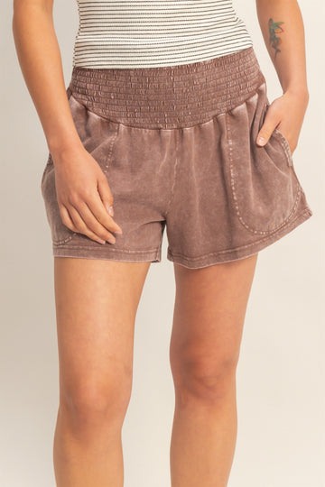 woman wearing brown smocked waistshorts with side pockets and a relaxed fit