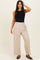 woman wearing a black fitted tank top and light beige wide-leg trousers, posing with one hand on her hair